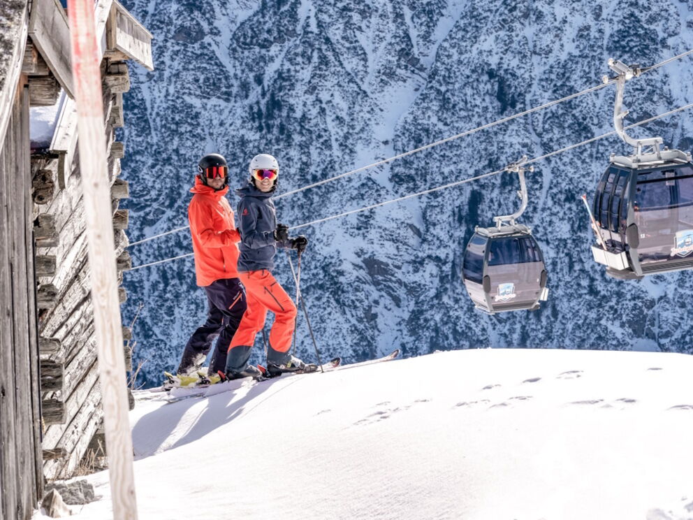 Zwei Skifahrer bei Sonnenschein vor dem Gondellift-Jöchelspitze.