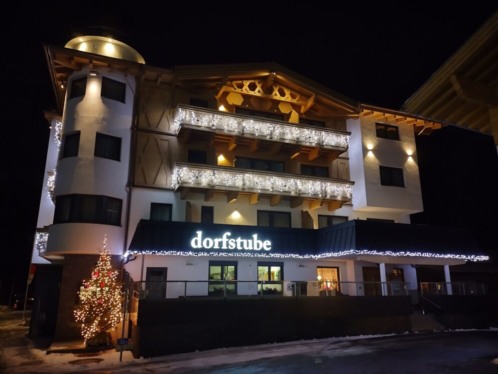Leuchtend, dekorierte Westseitenansicht im Winter und in der Nacht, der Dorfstube mit LED-Lichter.