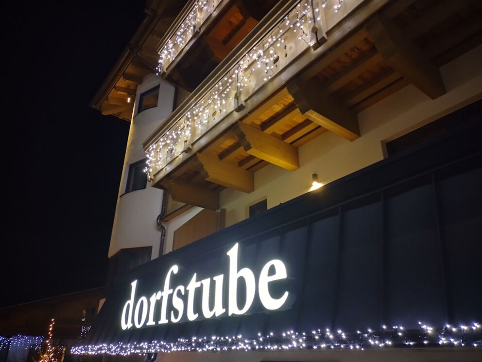 Schriftzug "Dorfstube" mit LED-Dekorationslicht an der Dachrinne.